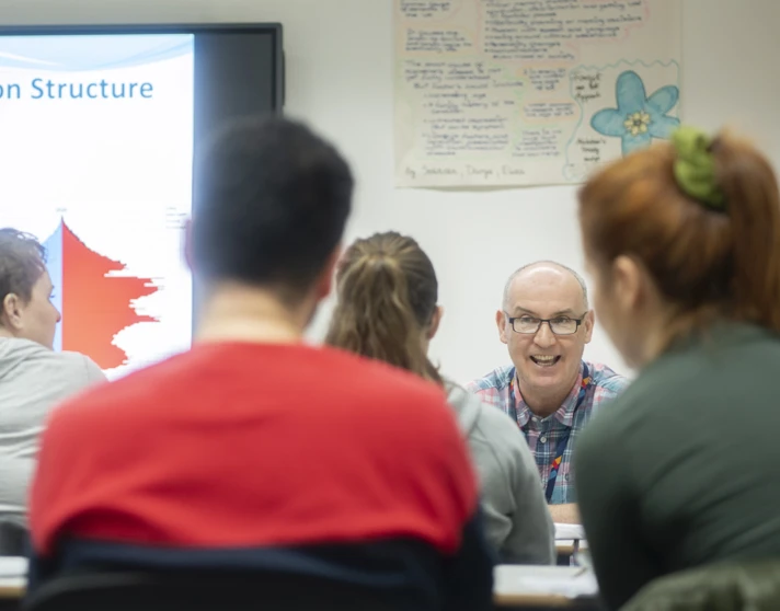 Lecturer smiling while teaching population structure in a lively classroom discussion. Lecturer smiling while teaching population structure in a lively classroom discussion.